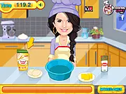 Screenshot of Selena Gomez Cooking Cookies game showing Selena in a kitchen, mixing ingredients for cookie dough with various baking tools visible.