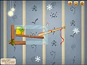 Gameplay screenshot of Gifts Pusher 2 showing a baseball bat positioned to push a wrapped Christmas gift across a cluttered room toward its target spot.