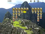 Gameplay screenshot of Machupicchu Invaders showing an Inca defender in the foreground, firing a spitting llama projectile at a row of advancing Spanish conquistador soldiers.